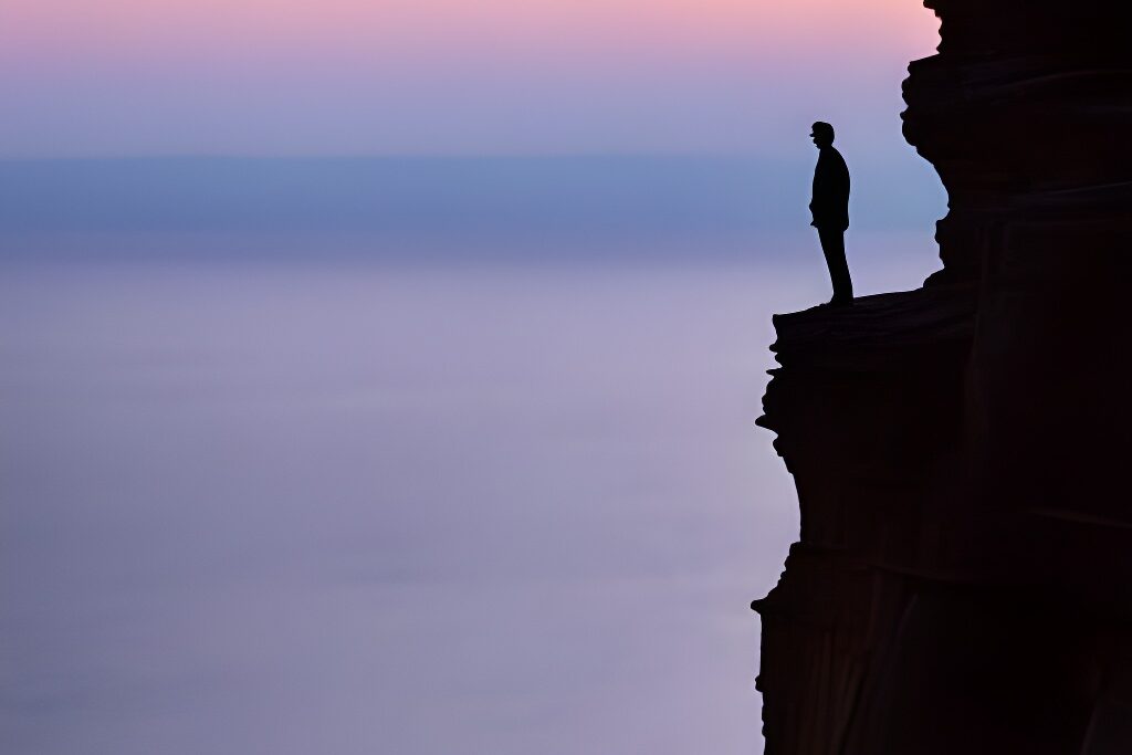 A solitary figure standing at the edge of a cliff, watching the sunrise, signifying a new beginning